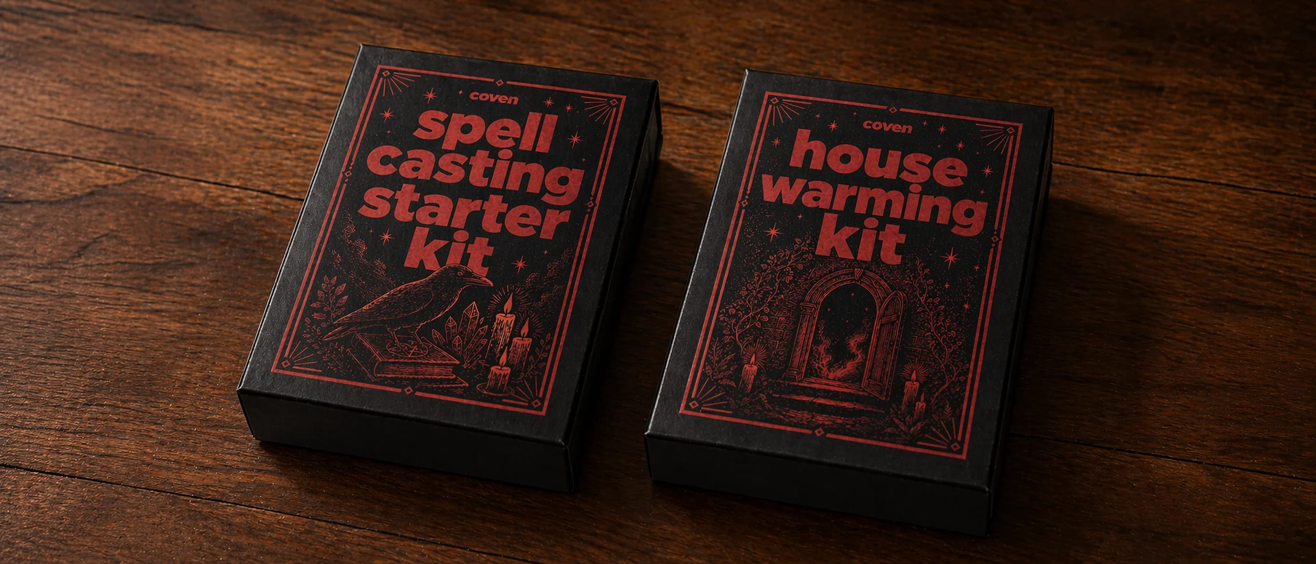 Two Coven spell kit boxes — the Spellcasting Starter Kit and the Housewarming Kit — in matte black with deep red ink illustrations, photographed side by side on a dark wood surface