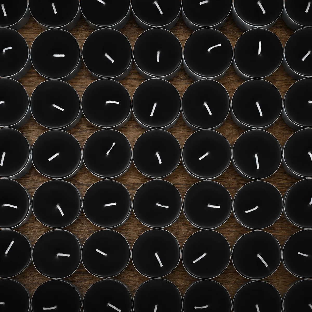 Candles in bulk — a top-down grid of black tea light candles on a dark wood surface