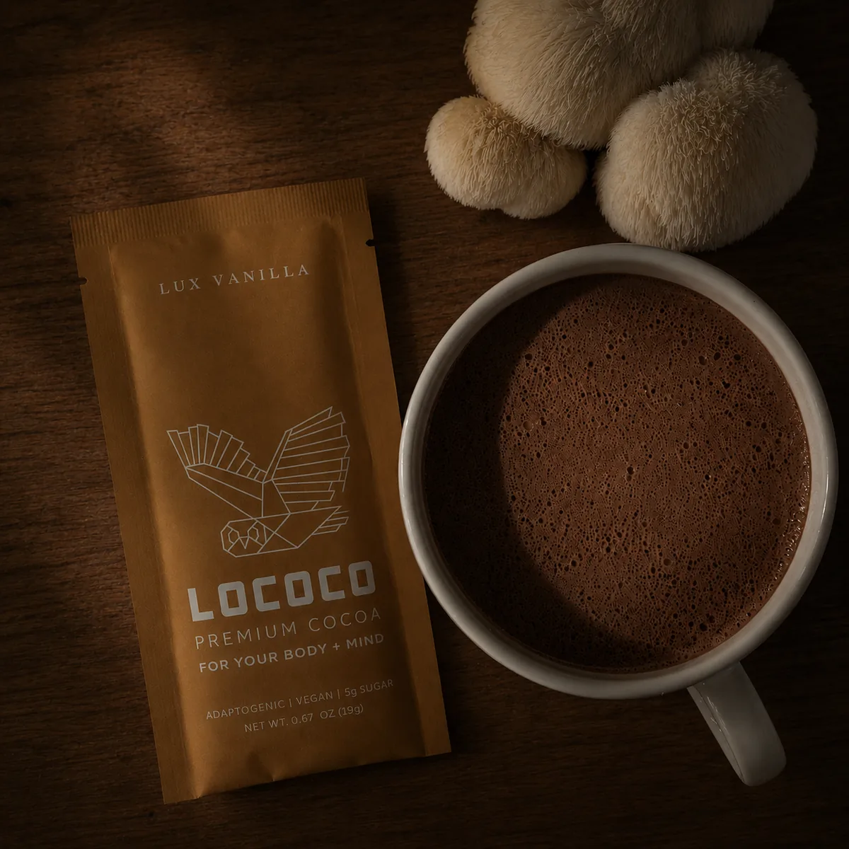 LOCOCO magic — a Lux Vanilla cocoa sachet in copper foil with the LOCOCO bird mark, beside a stoneware mug of foamy hot cocoa and a cluster of lion's mane mushrooms on a dark wood surface