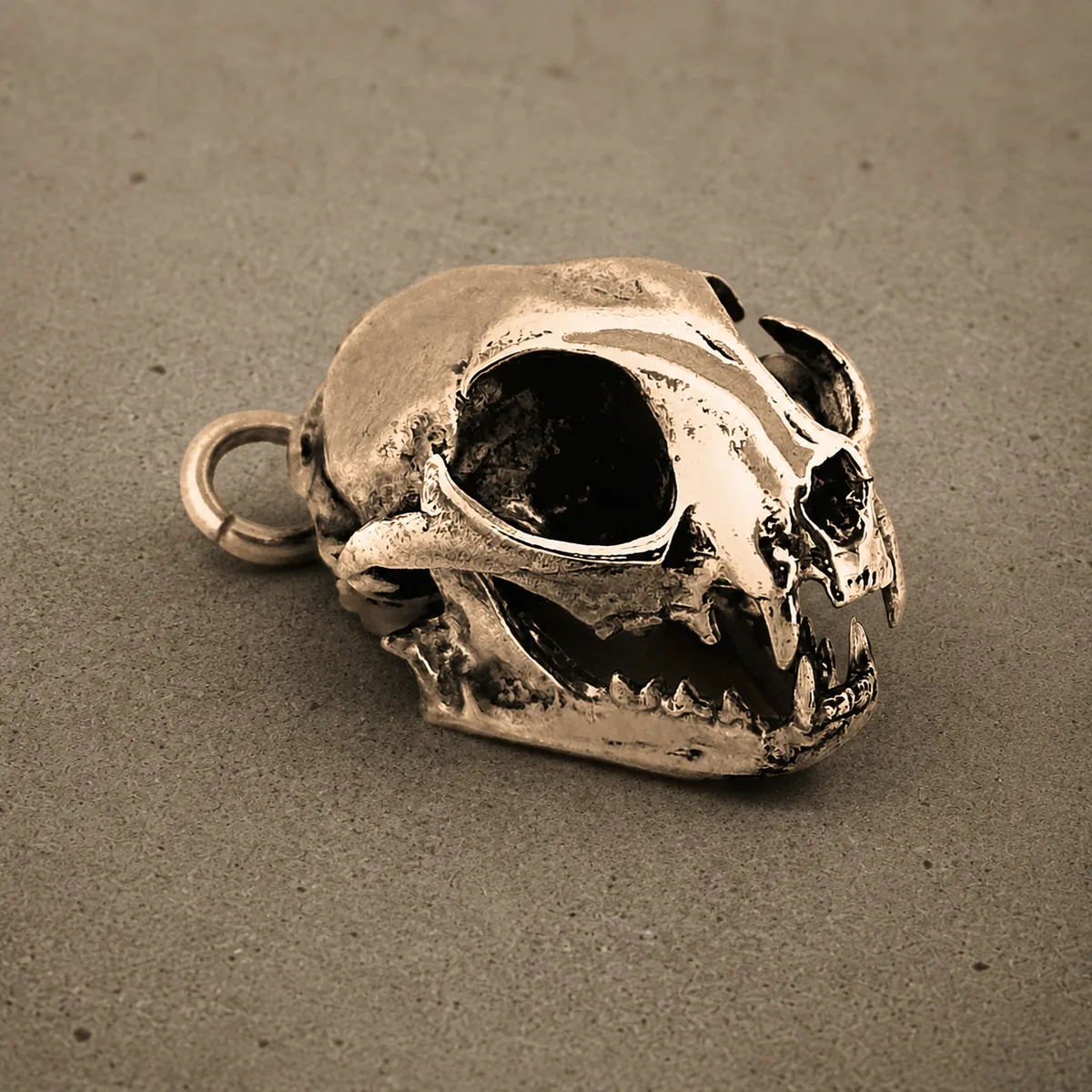 Yellow bronze cat skull pendant with bared fangs, photographed against a concrete surface