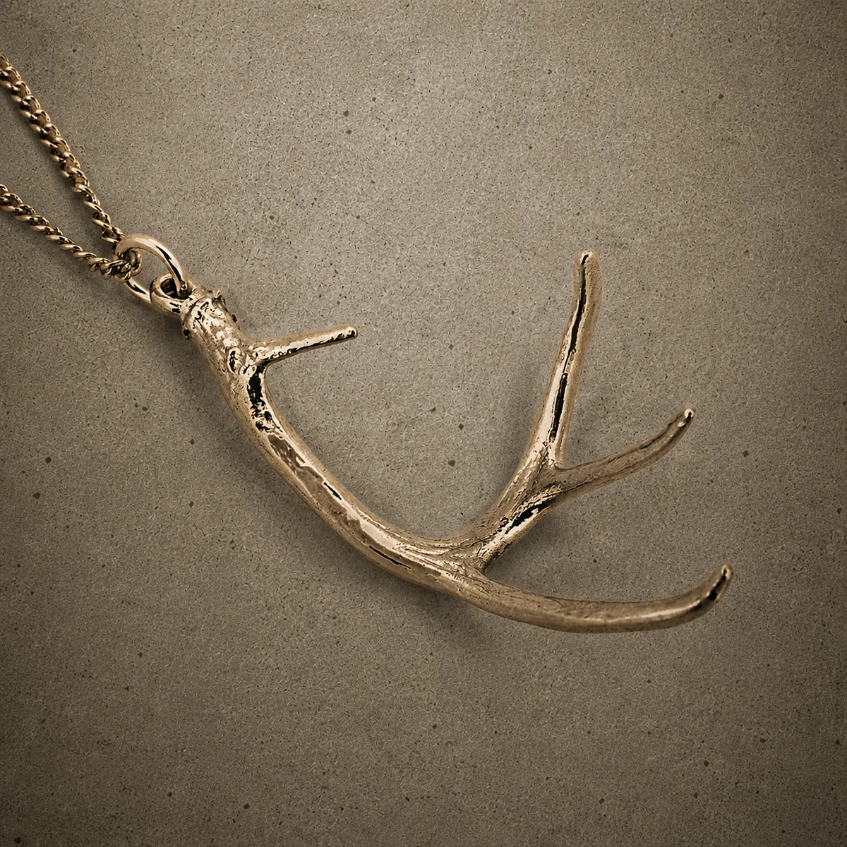 Yellow bronze deer antler pendant on a chain, photographed against a concrete surface