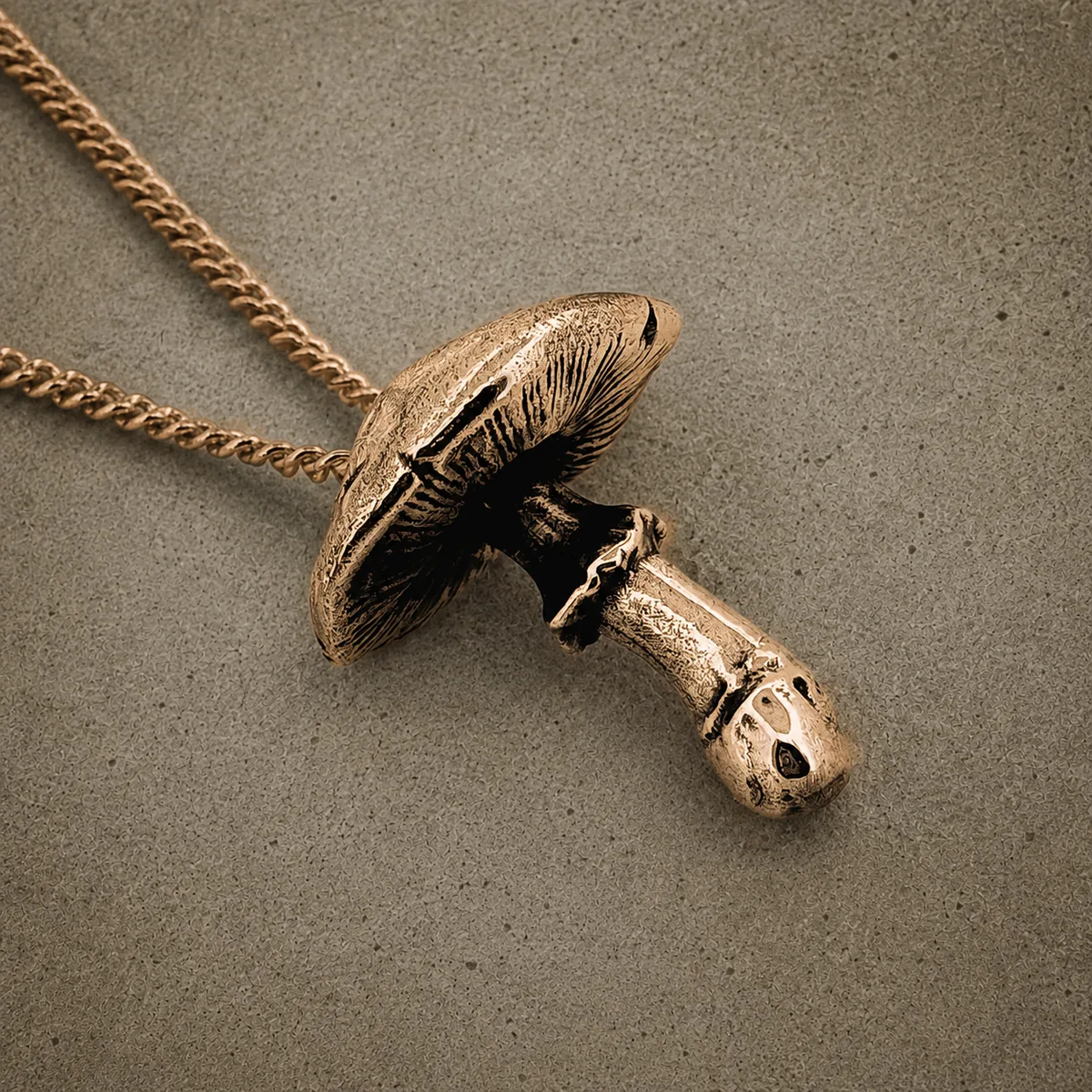 Yellow bronze fly agaric mushroom pendant on a chain, photographed against a concrete surface
