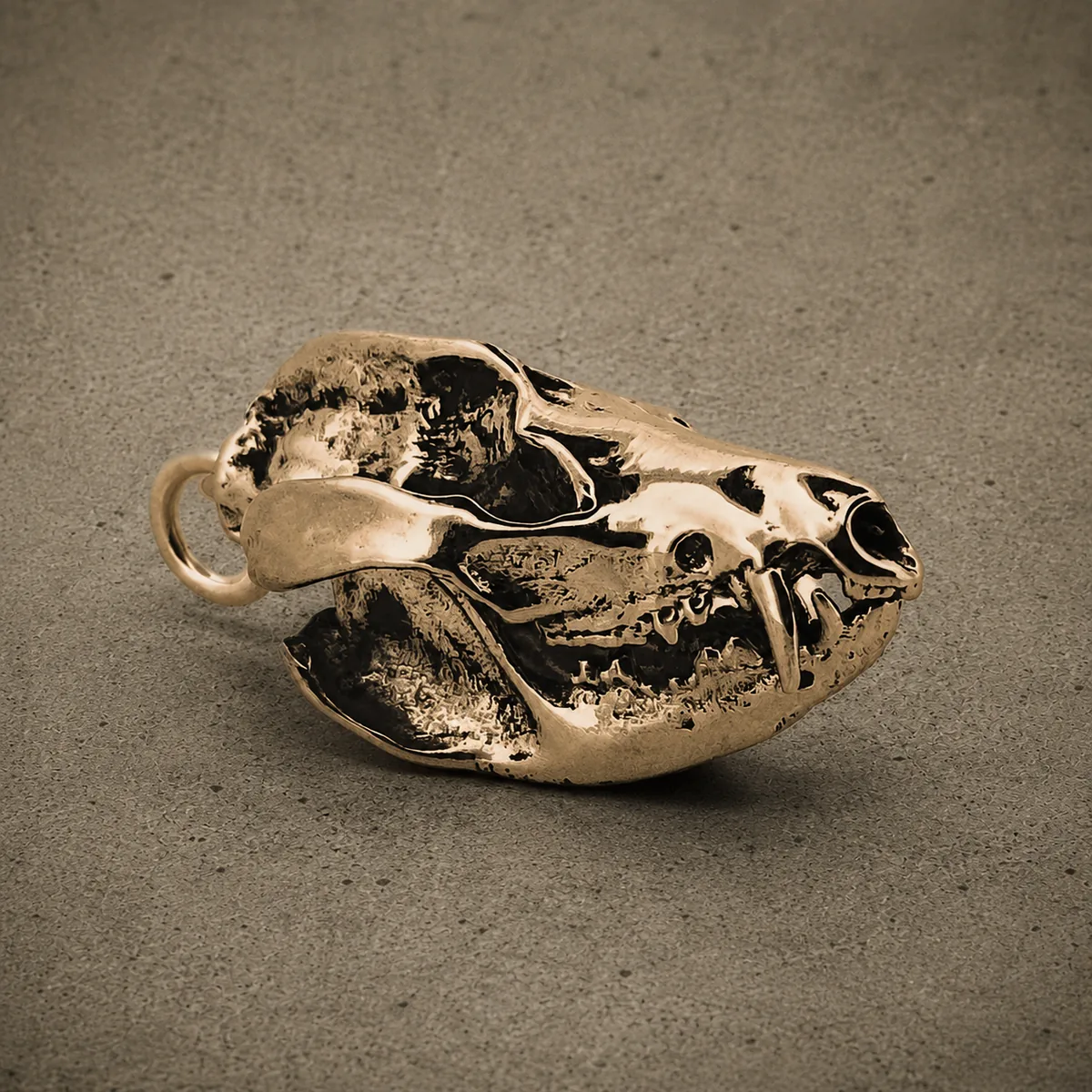 Yellow bronze opossum skull pendant with a hinged jaw and bared teeth, photographed against a concrete surface