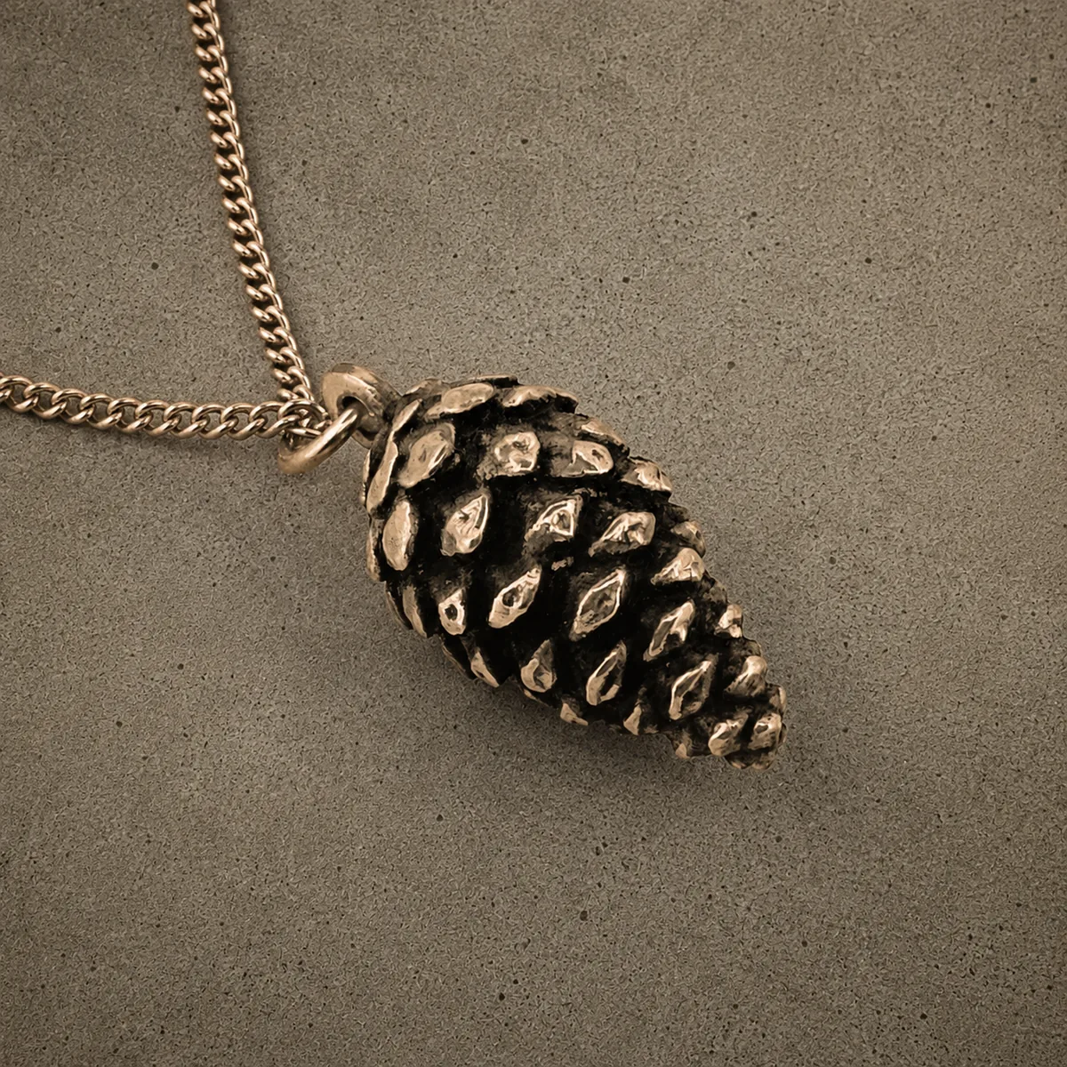 Yellow bronze pinecone pendant on a chain, photographed against a concrete surface
