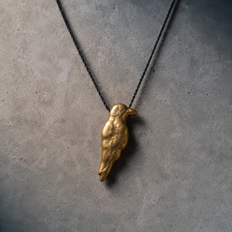 Raven talisman — a cast brass raven pendant on a blackened chain, photographed against a concrete surface