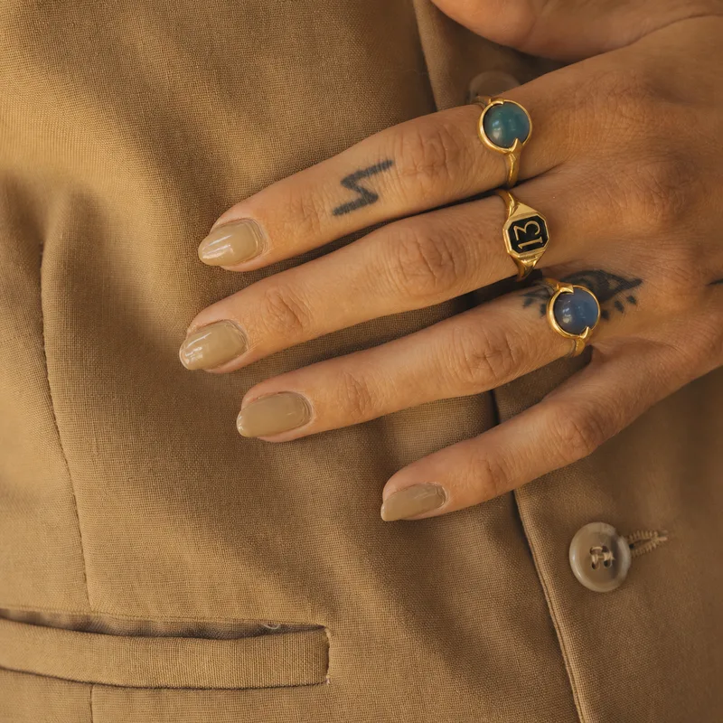 Moody ring — worn on a hand resting against a camel blazer, alongside a '13' signet ring